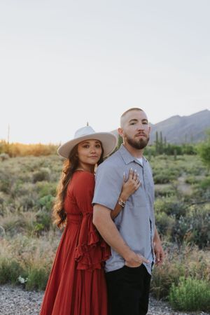 A couple poses back-to-back in a desert setting during golden hour.