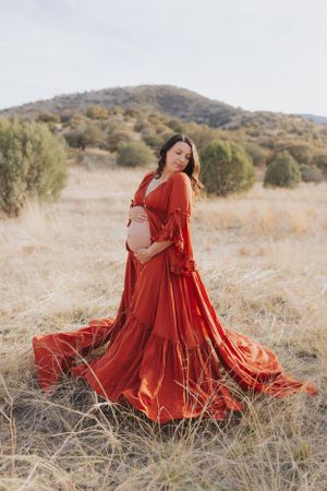 Dramatic red maternity gown flows in desert landscape with mountains in background.