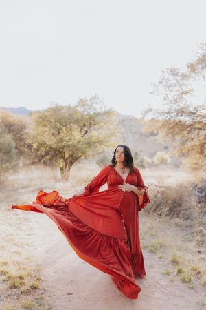 Vibrant red dress catches wind on desert trail with mountains and trees in background.