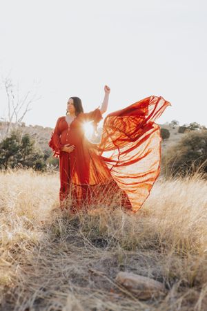 Sunset maternity photo with flowing red dress catching golden light in desert setting.