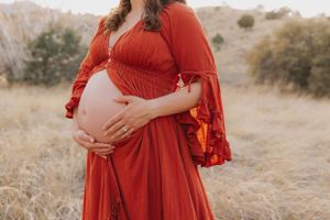 Close-up maternity portrait showing flowing red dress details against desert background.