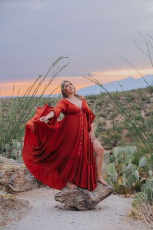 A flowing red dress catches the wind on a rocky desert trail during sunset.