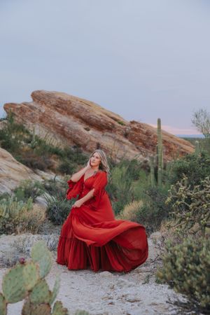 A red dress twirls against desert rock formations and saguaro cacti at dusk.