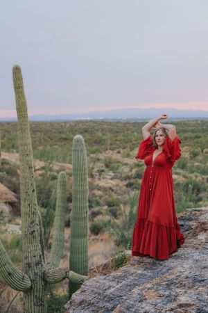 A flowing red dress stands out against tall saguaro cacti and desert landscape at sunset.