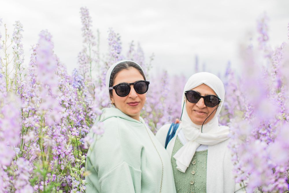 Adult mum and daughter pose together in a field of blooming purple delphinium flowers on a sunny day by Hayley Elizabeth photography