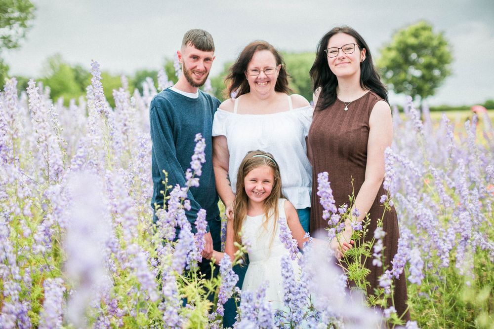 A family stands together in a beautiful field of blooming lilac flowers on a bright summer day at confetti fields by Hayley Elizabeth photos