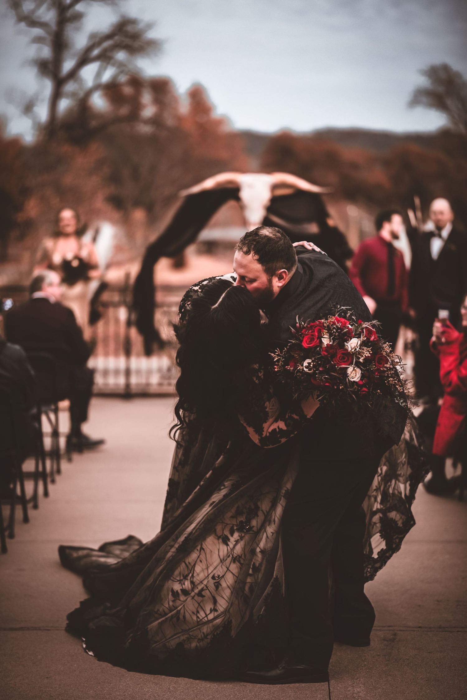 A couple shares an intimate moment at their outdoor wedding while wearing dramatic black wedding attire.