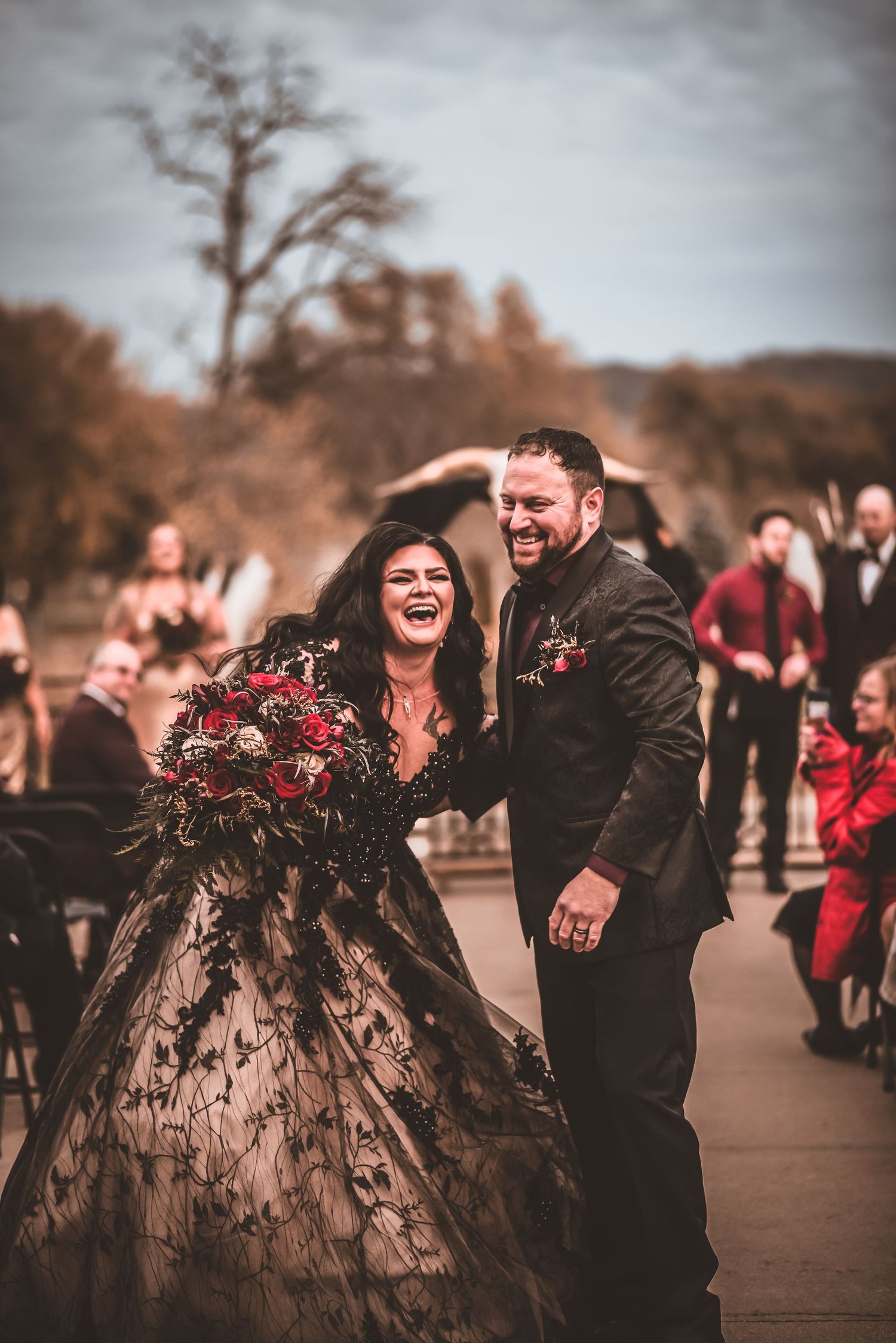 A joyful wedding moment captured outdoors with the couple laughing together in black formal attire.