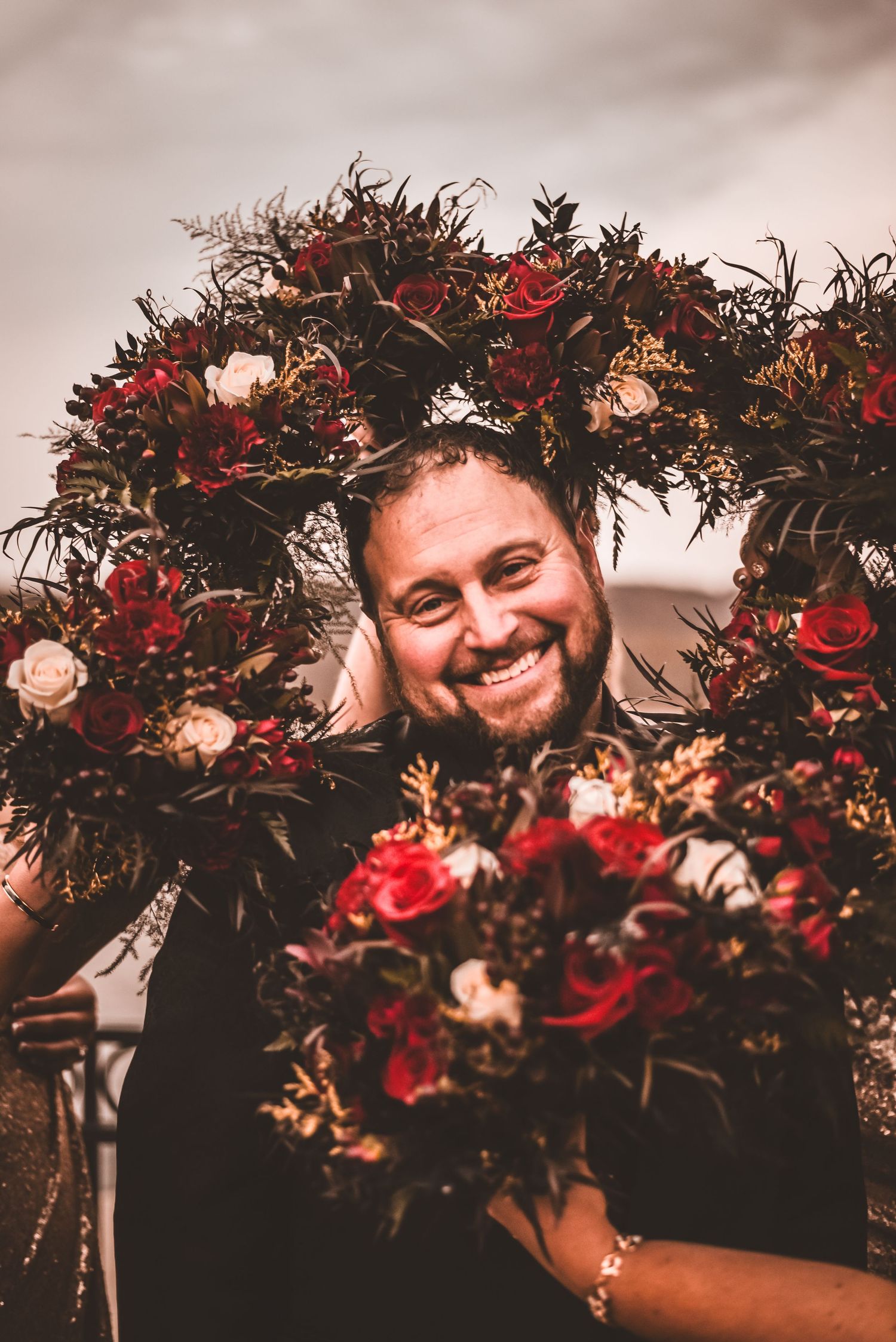 Beautiful floral wreath with red roses frames joyful moment at outdoor wedding.