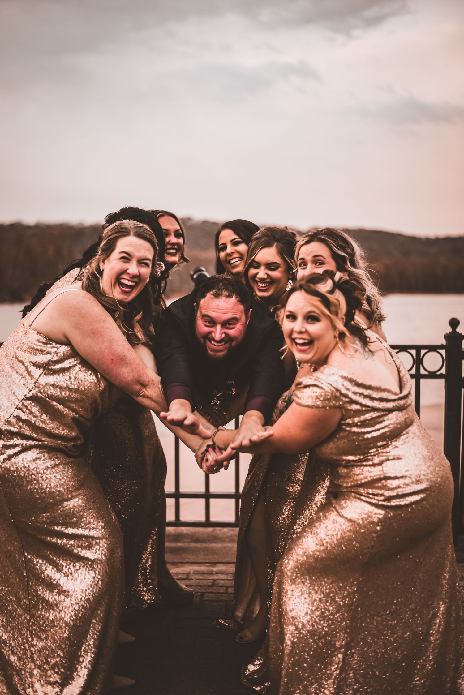 Bridesmaids in gold sequin dresses share fun moment at waterfront wedding venue.