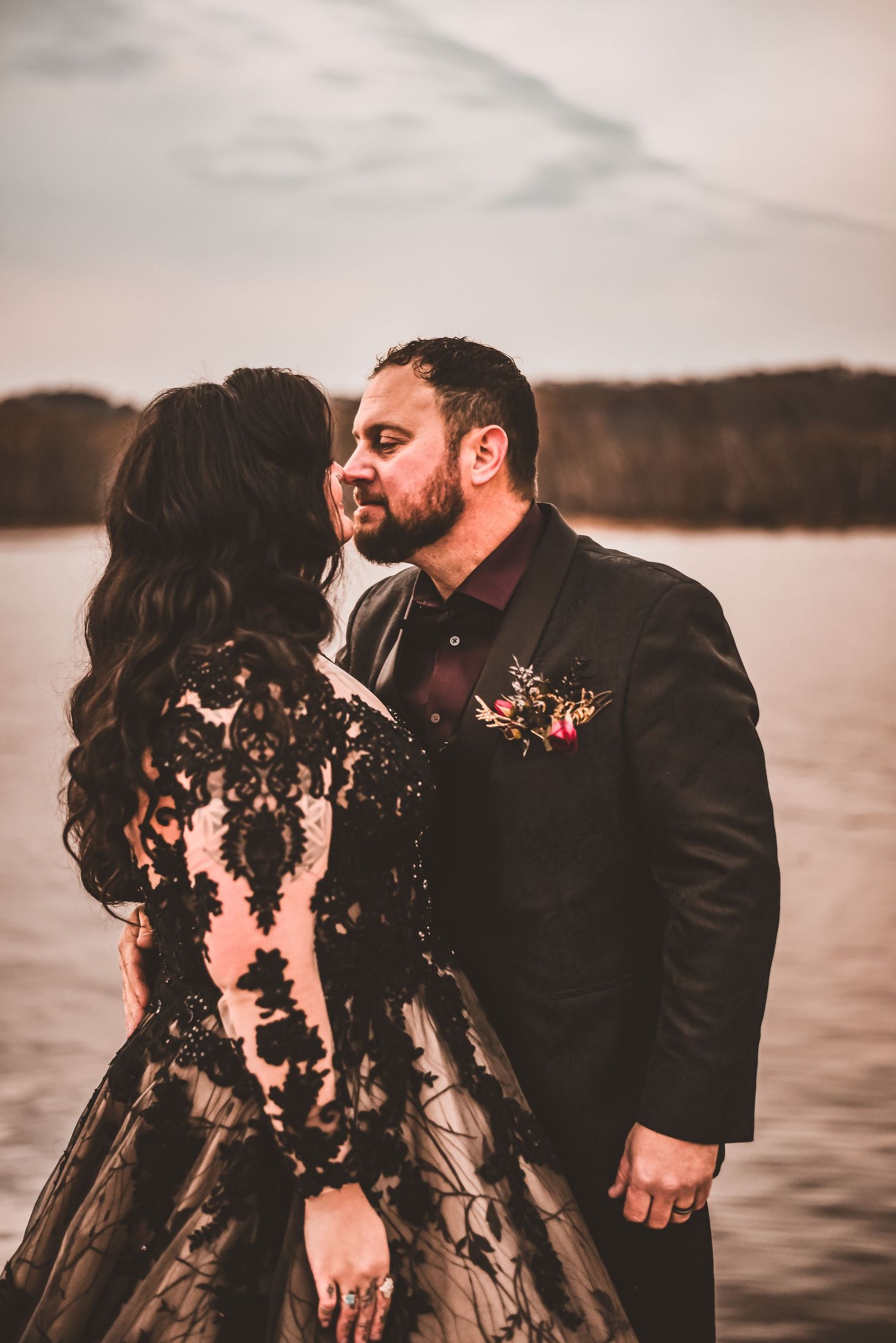 A romantic waterfront wedding photo featuring a couple in black formal attire.