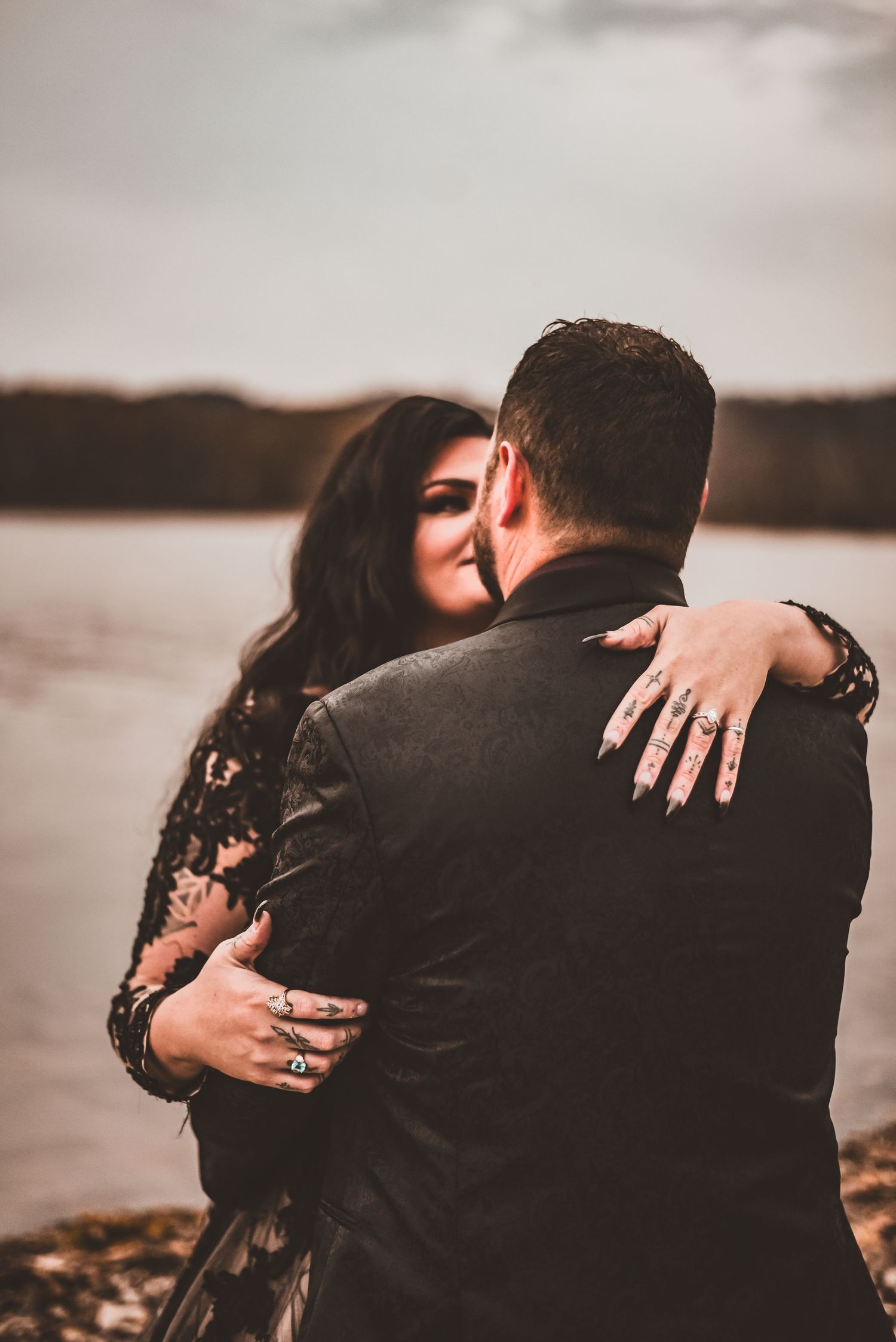 A tender embrace captured from behind showing the details of a black lace wedding dress.