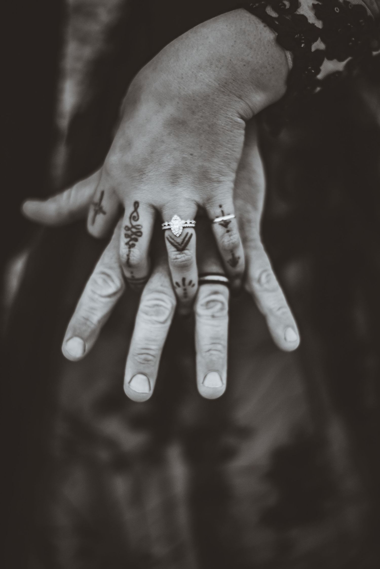 A black and white close-up of a hand displaying multiple ornate wedding rings.