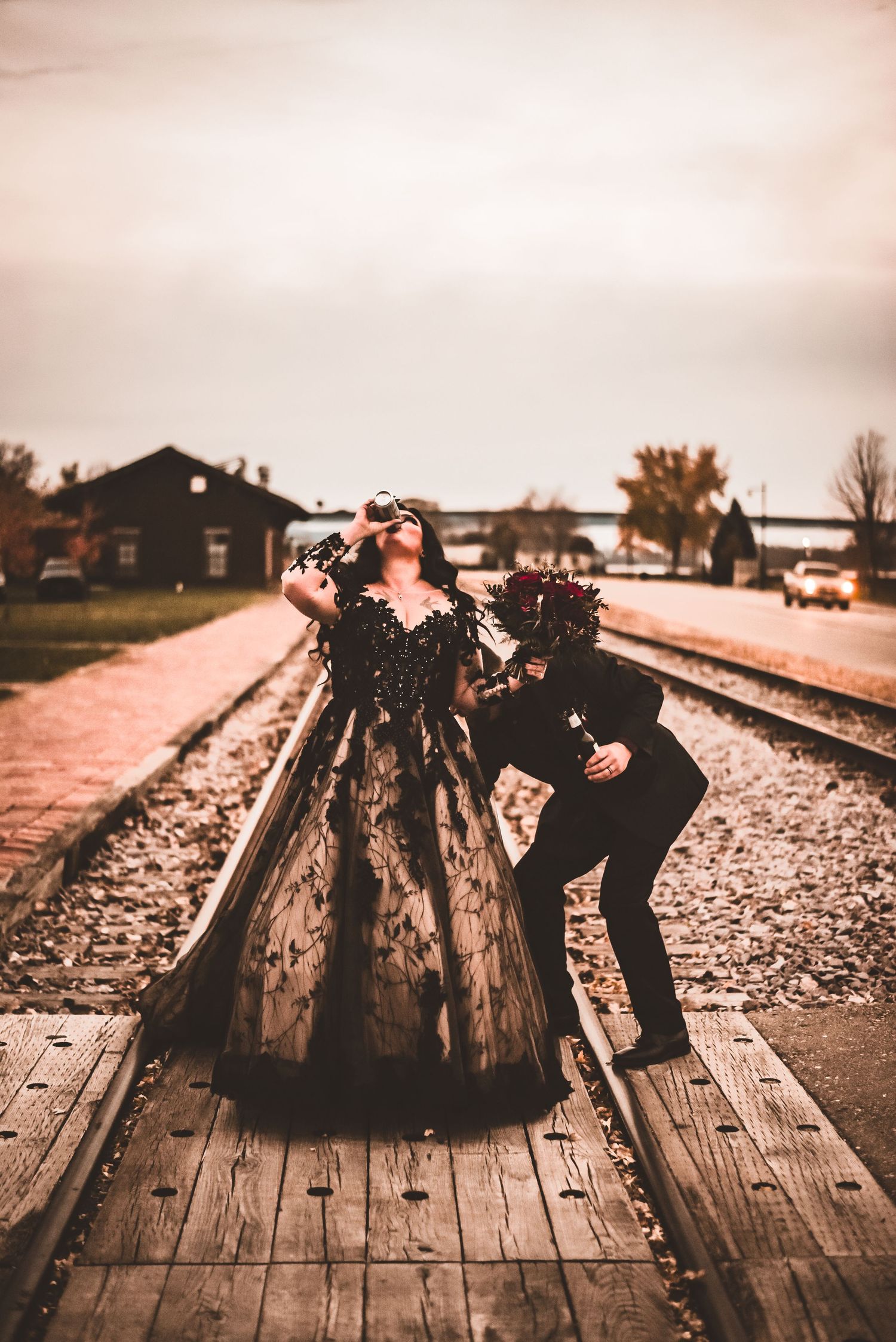 A playful photo shoot on railroad tracks with a couple dressed in formal black attire.