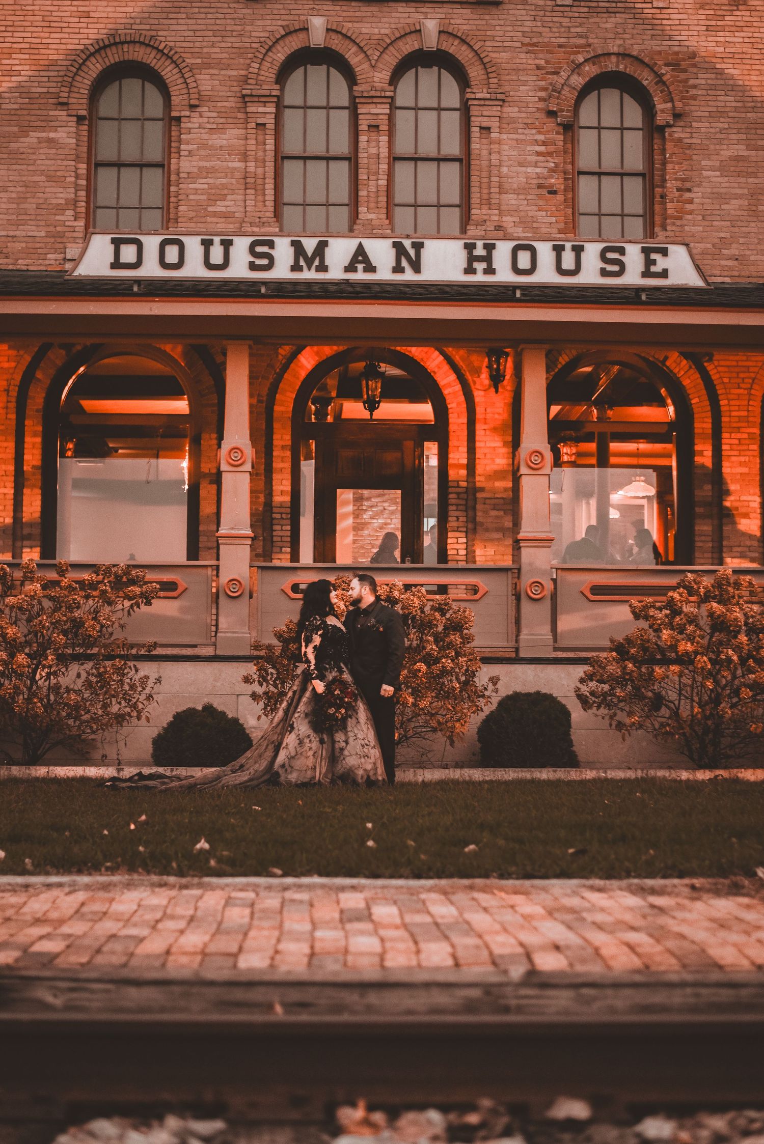 A couple poses romantically outside the historic Dousman House building at dusk.