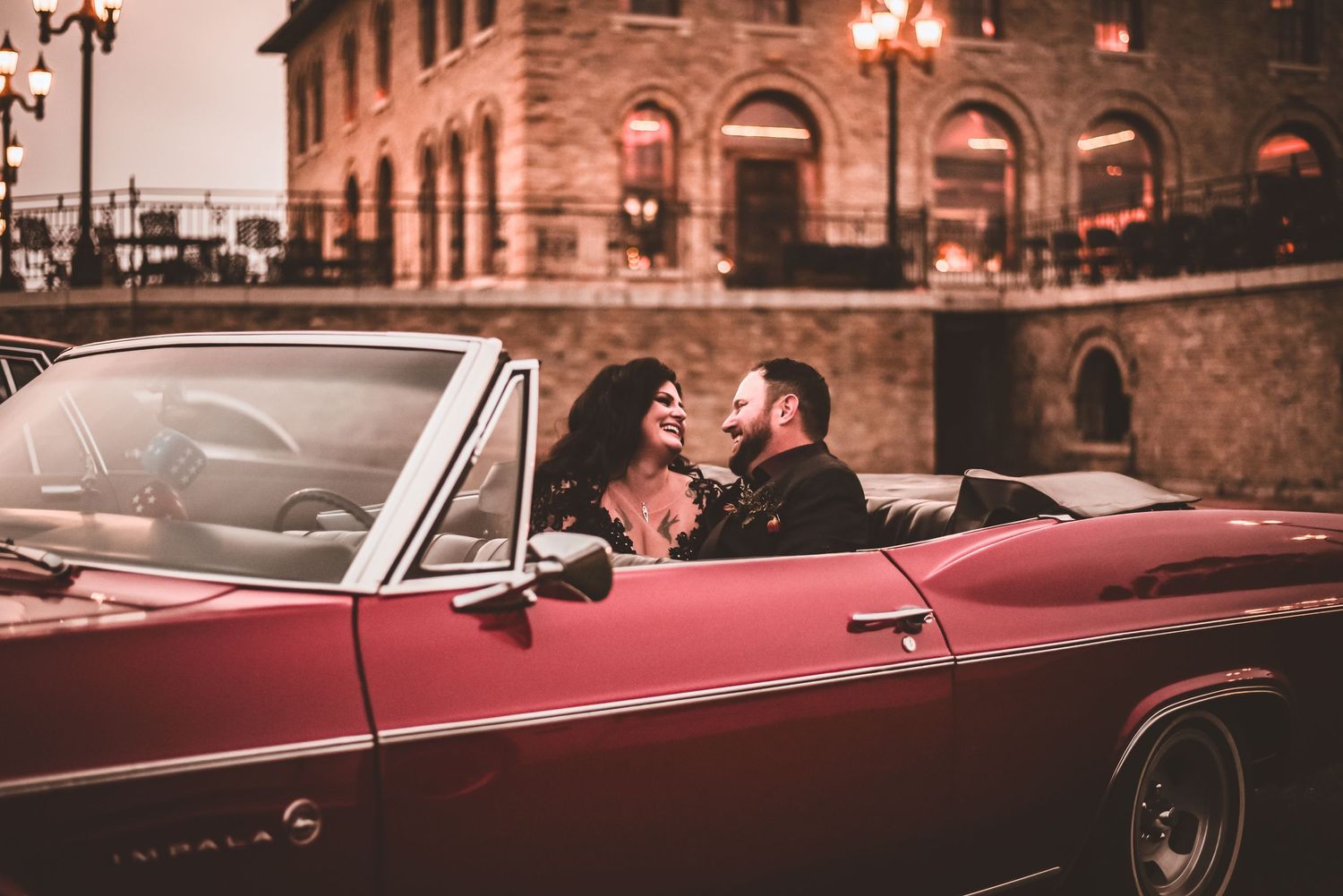 A romantic moment in a vintage red convertible car against historic architecture.