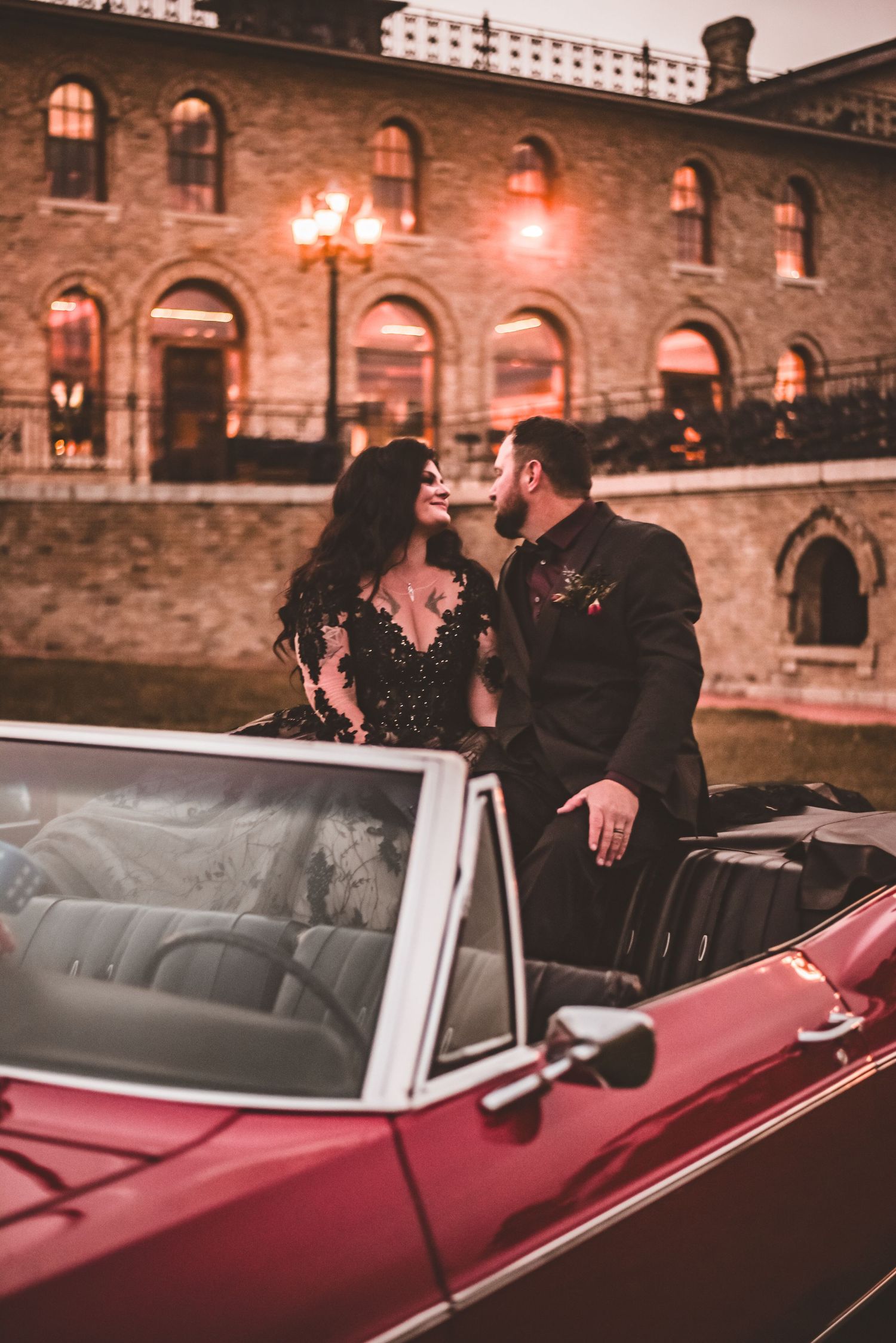 A romantic photo in a classic red convertible against a historic brick building backdrop.