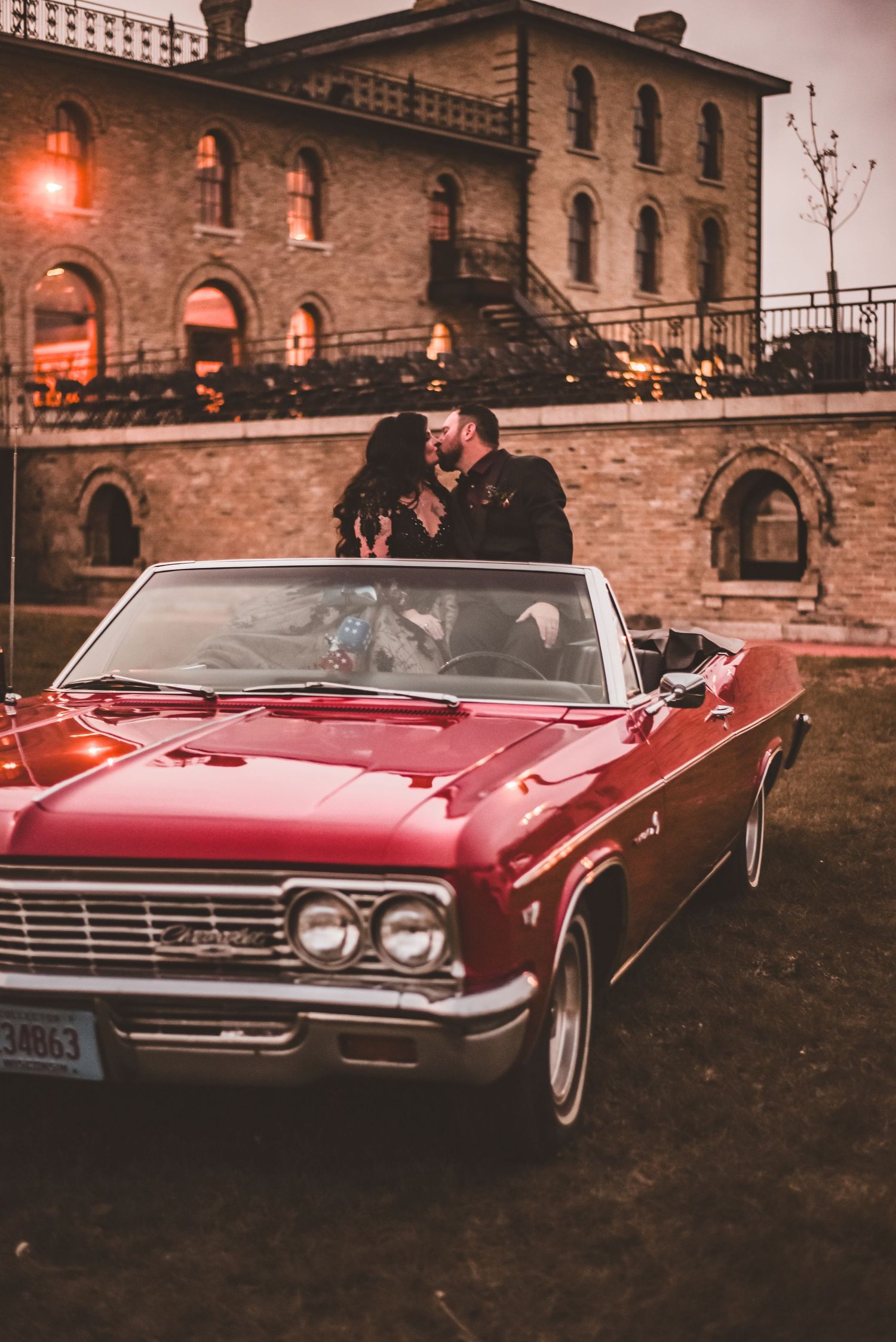 A vintage red Chevrolet convertible parked in front of a historic brick building at dusk.