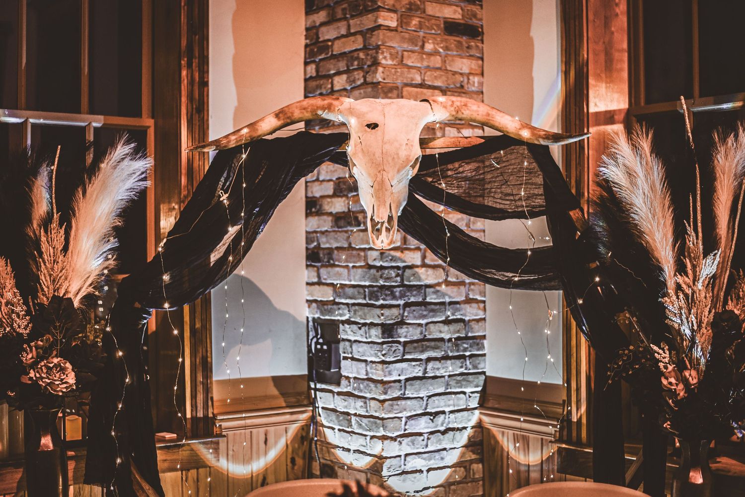 Rustic wedding decor featuring a cattle skull and pampas grass against a stone wall.