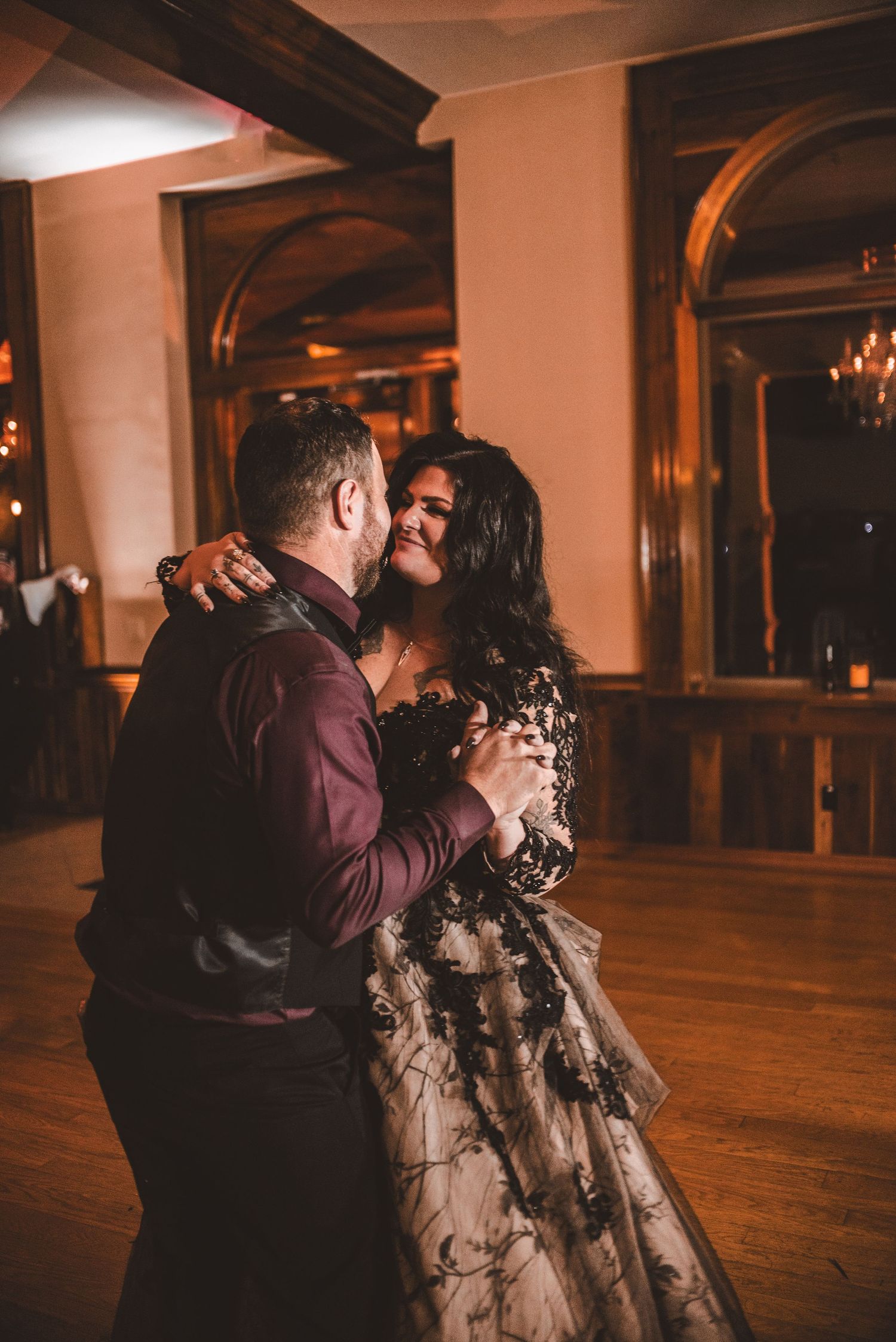 A romantic dance moment captured in a warmly lit ballroom with arched windows.