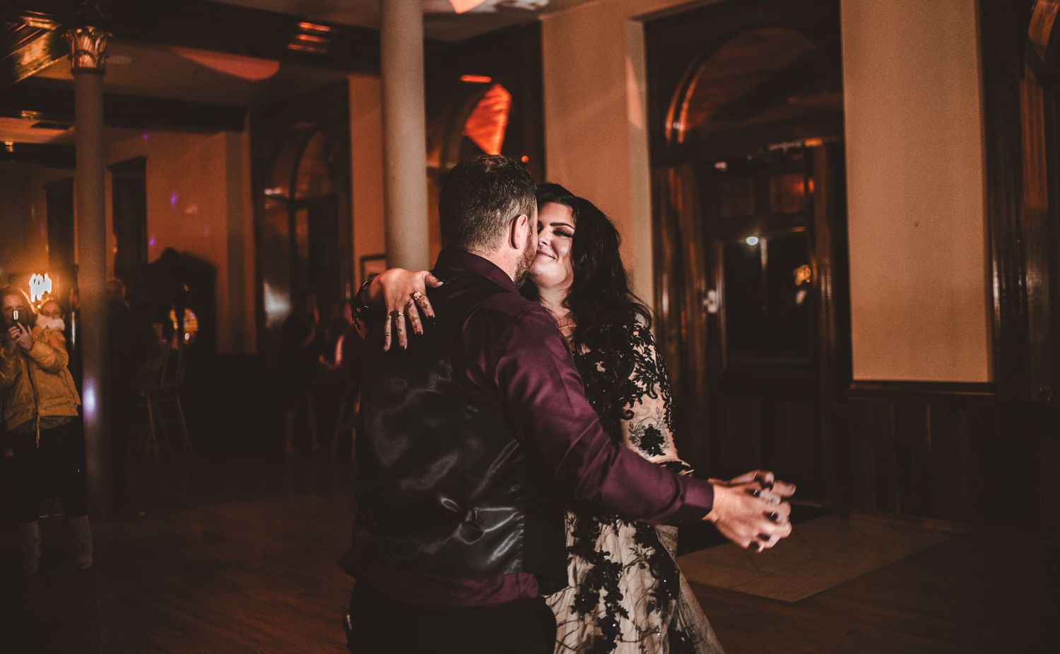 A couple embraces during their dance in a romantic ballroom setting with warm lighting.