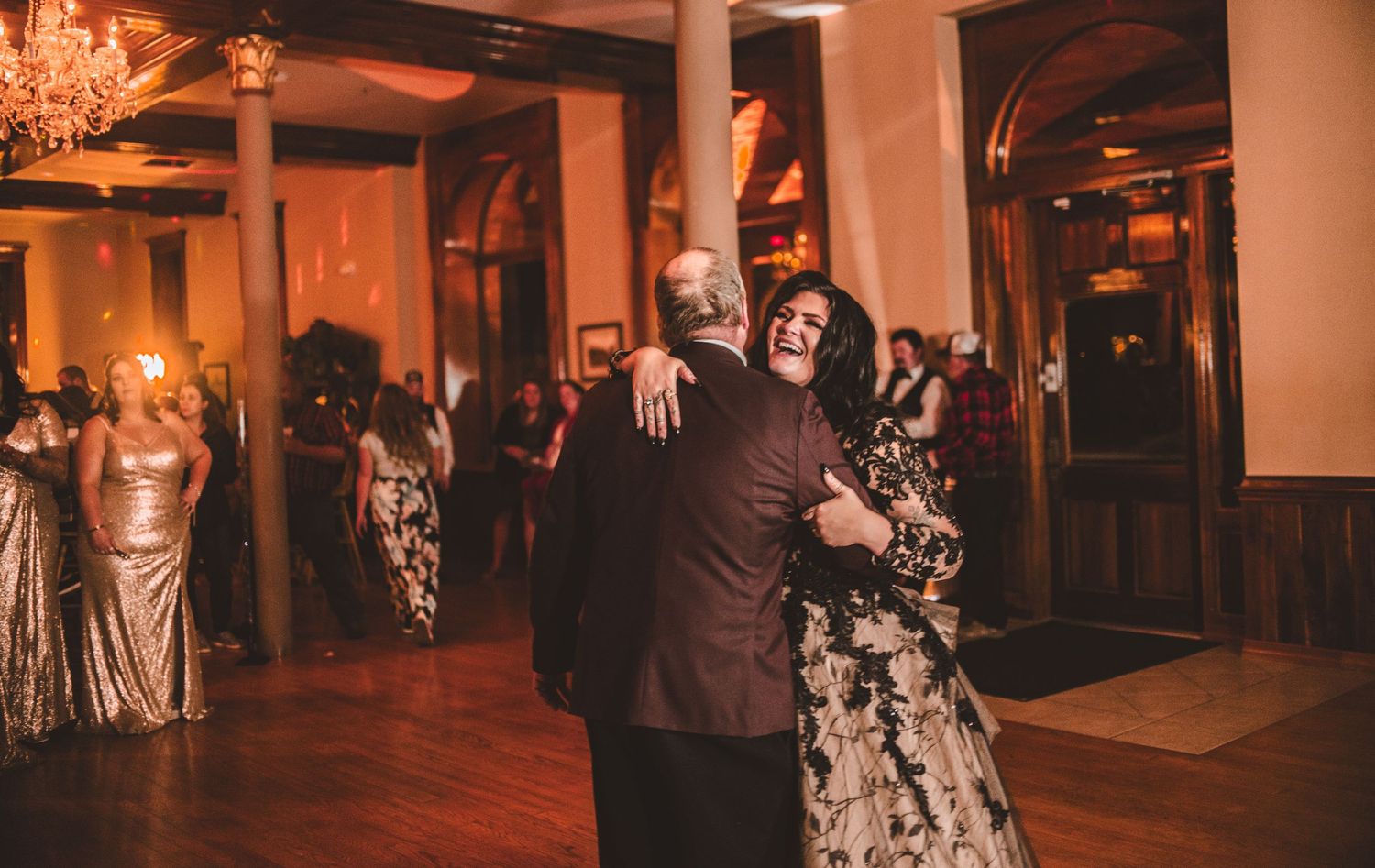 A couple shares an emotional dance moment in an elegantly lit ballroom setting.