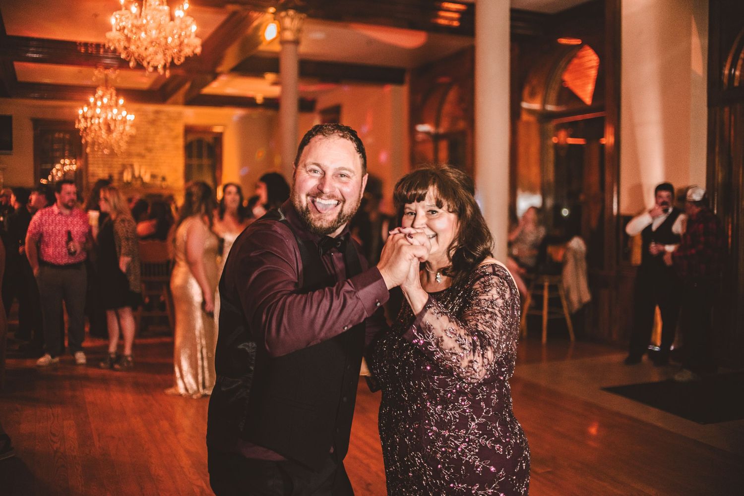 Joyful couples dancing together at an elegant reception venue with sparkling chandeliers overhead.