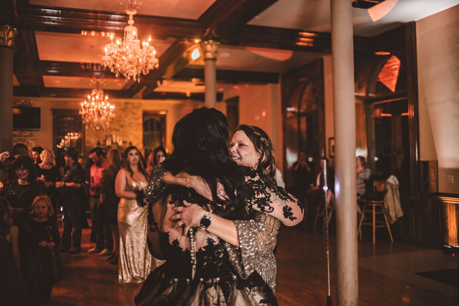 Couples dancing in an elegant ballroom with chandeliers and exposed brick walls.