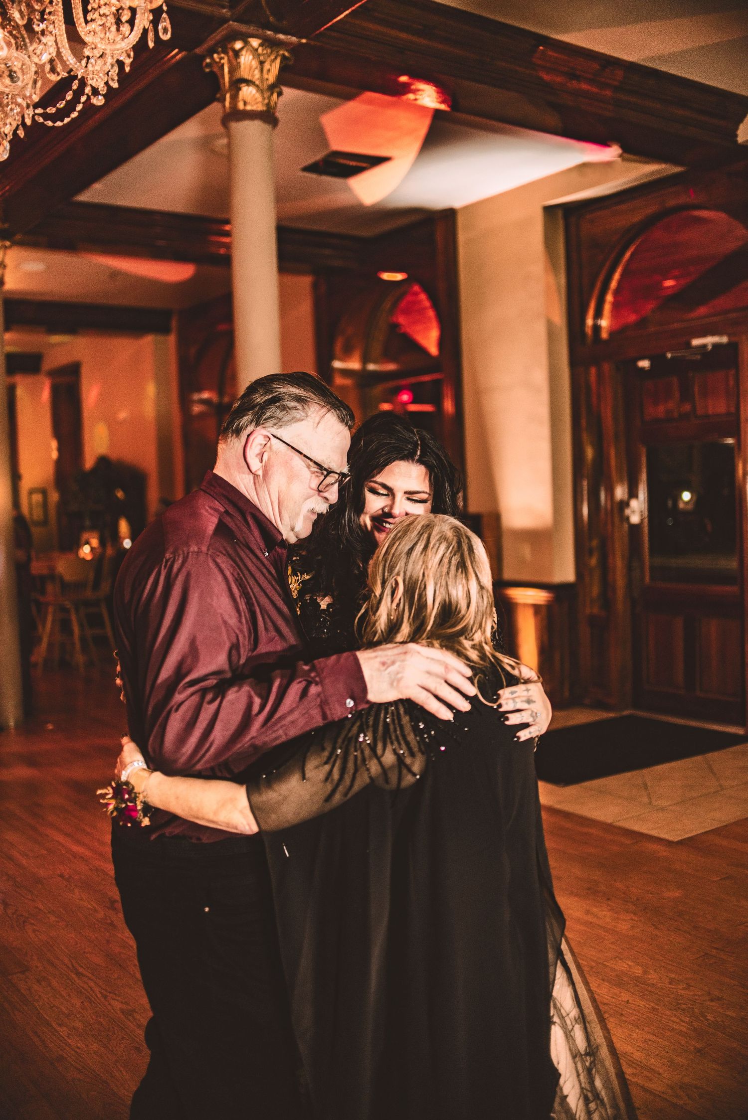Three people share an intimate dance moment at an elegant indoor reception.