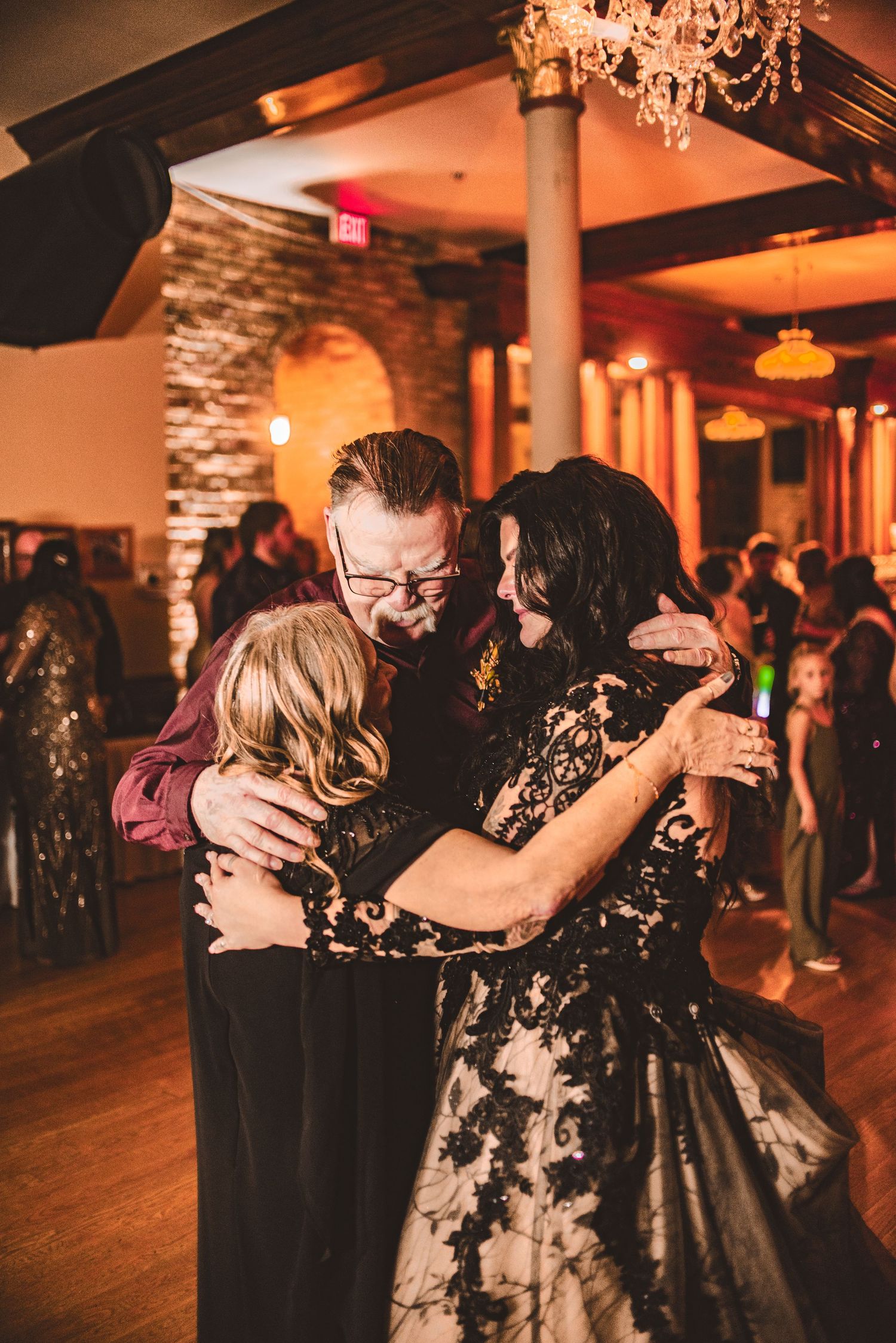 Group embrace during a dance at an elegant indoor venue with exposed brick walls.