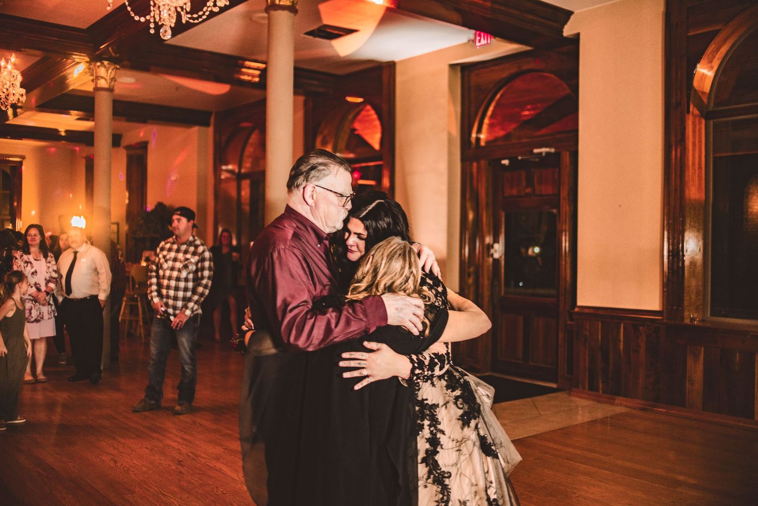 Three people dancing together at an indoor reception with warm lighting.