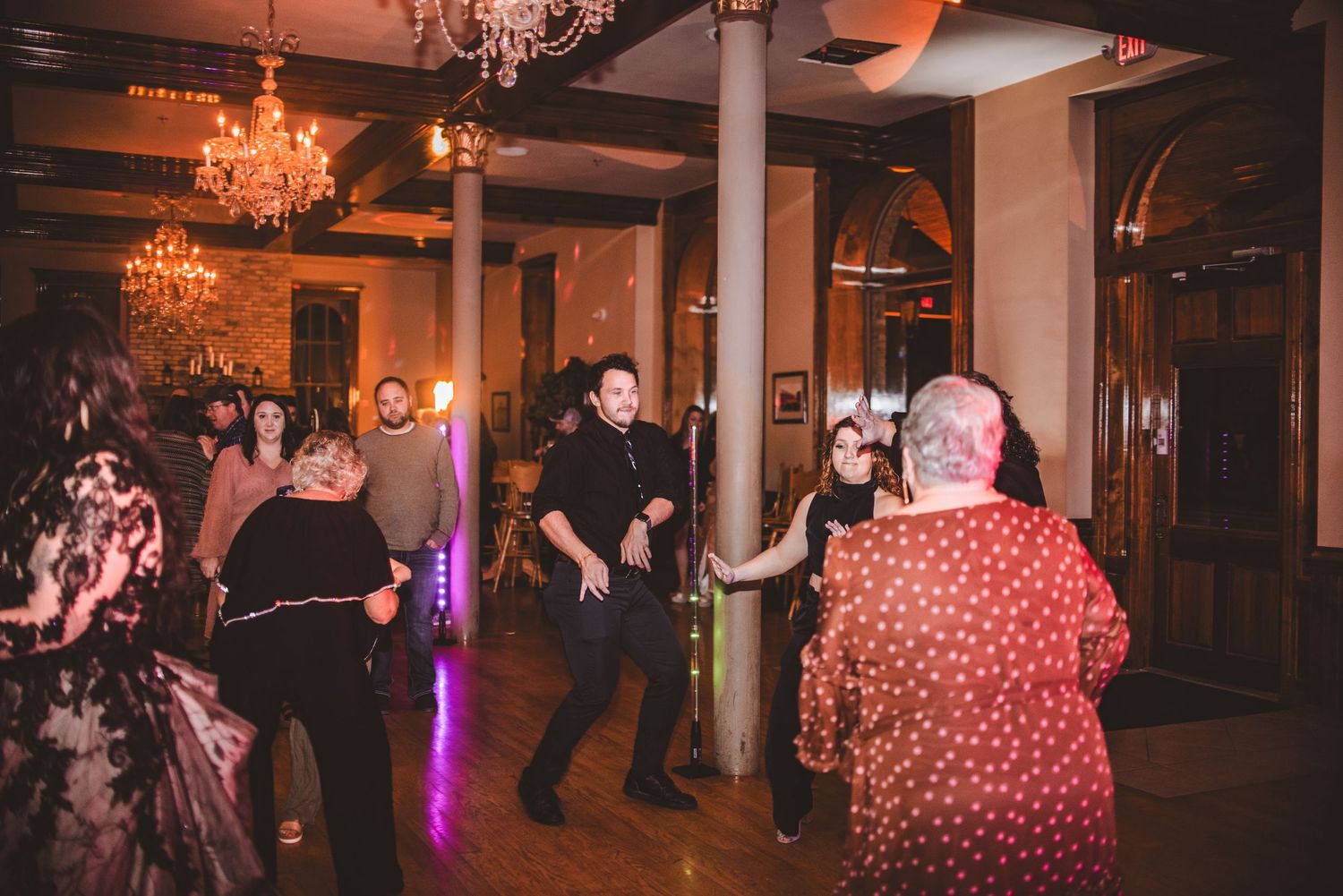 People dancing and celebrating in an elegant ballroom with crystal chandeliers.