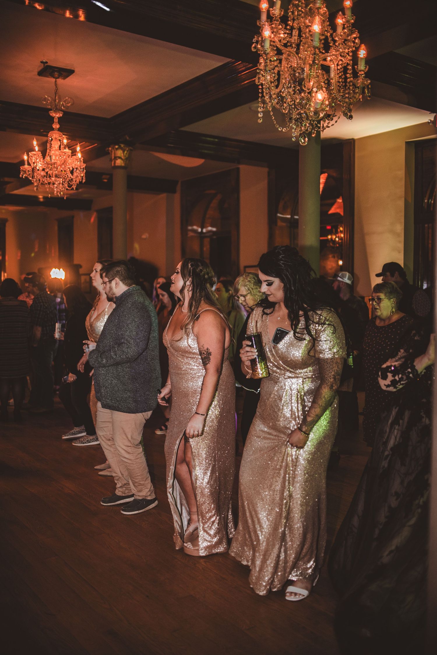Group of guests in formal attire dancing under ornate chandeliers at an evening event.