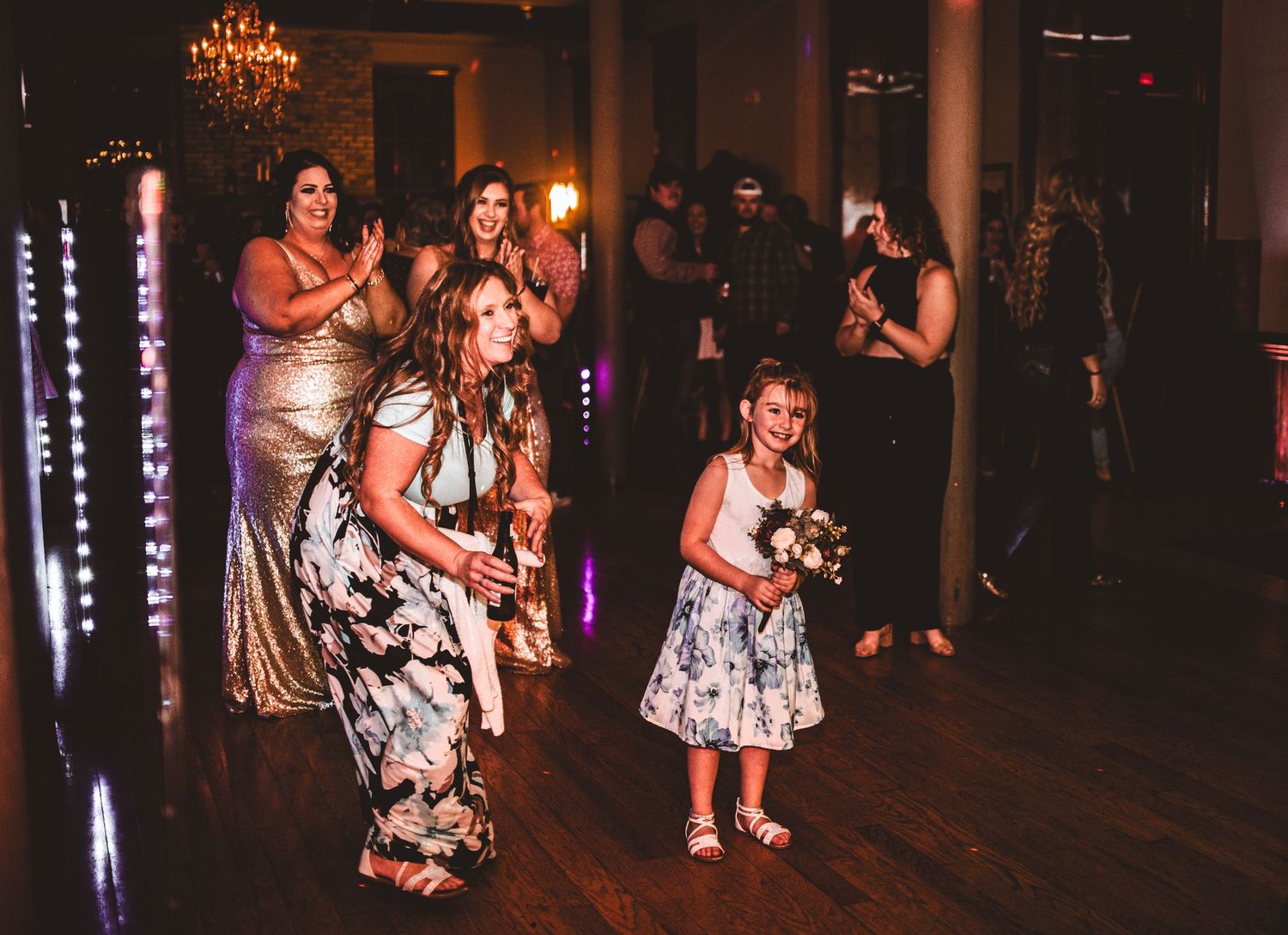 Group dancing at formal event with crystal chandeliers and mood lighting.