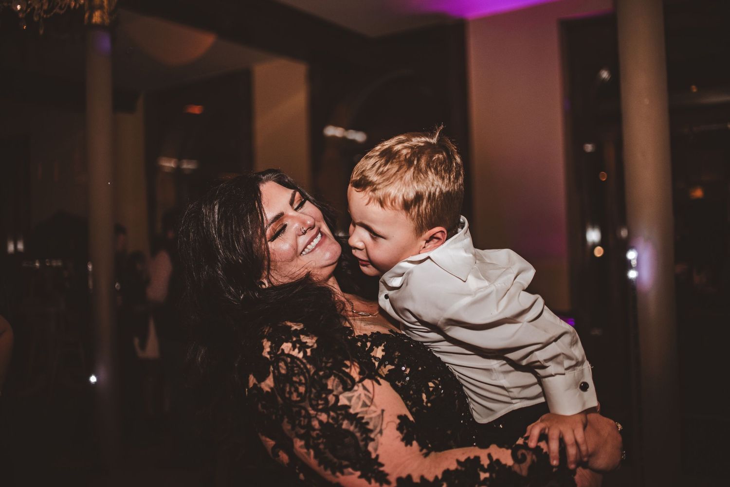 Mother and child share a loving embrace during a wedding reception with purple lighting.