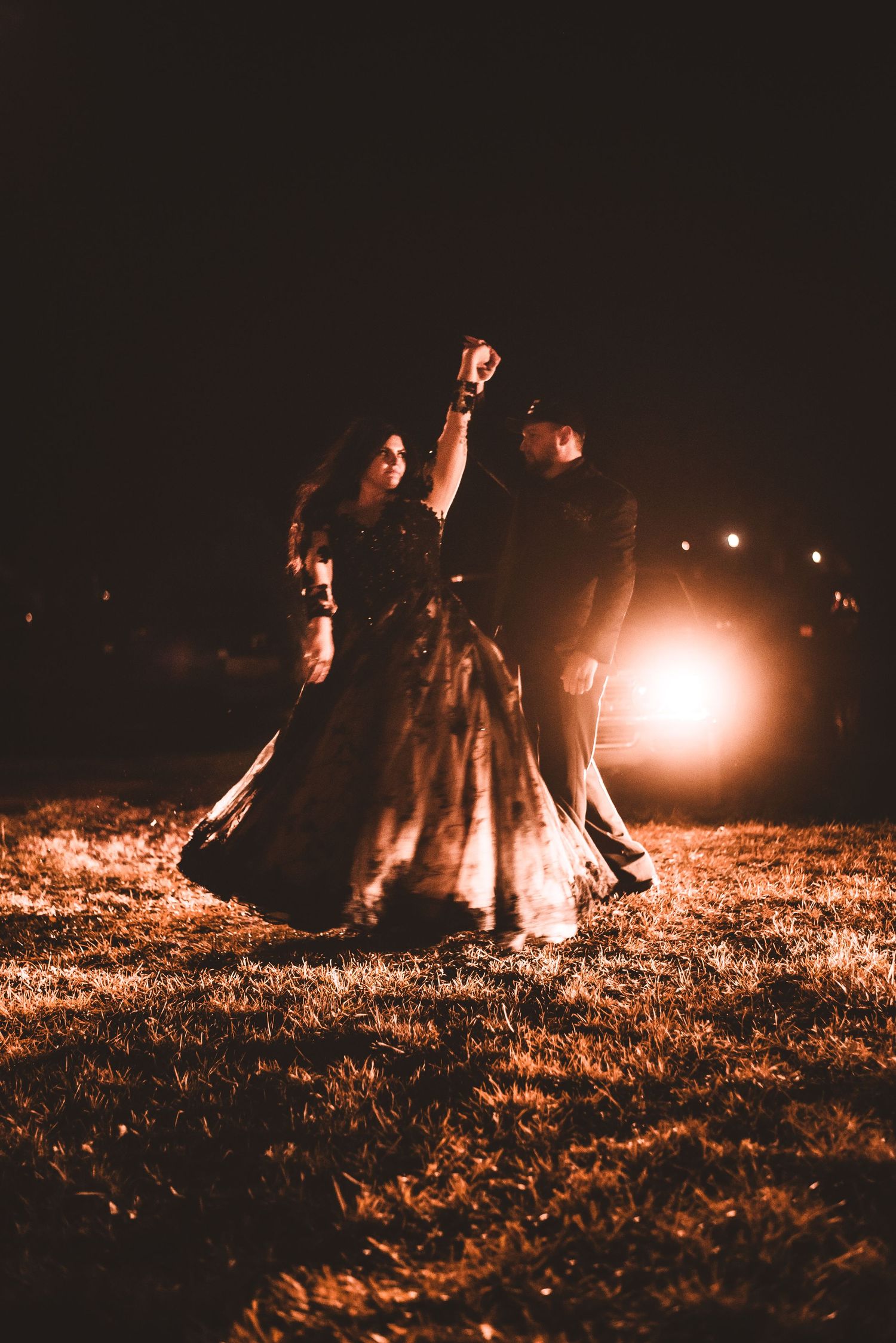Formal dancing silhouettes against car headlights in a dark outdoor setting.