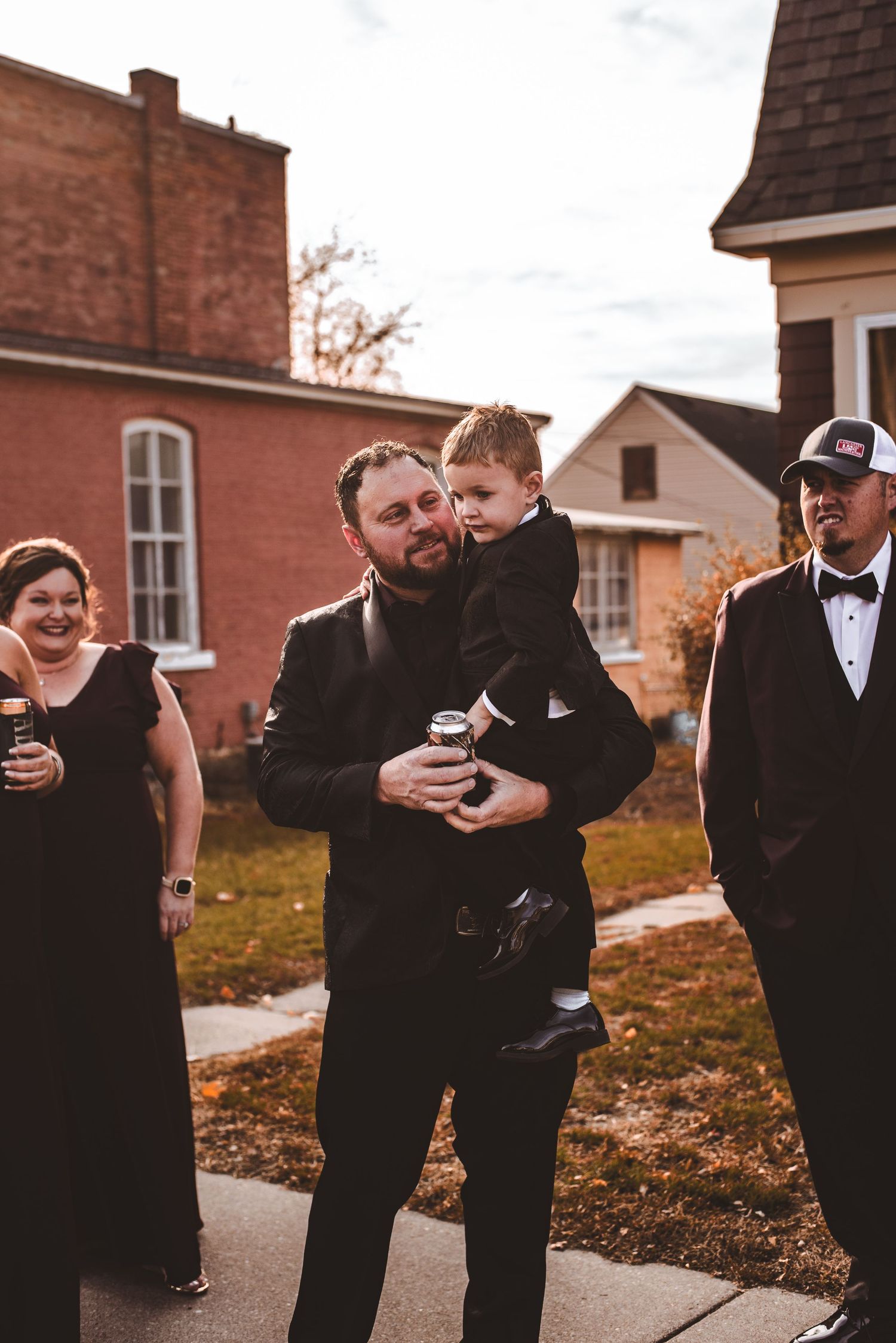 Wedding party members in formal attire gathered outside a brick building.