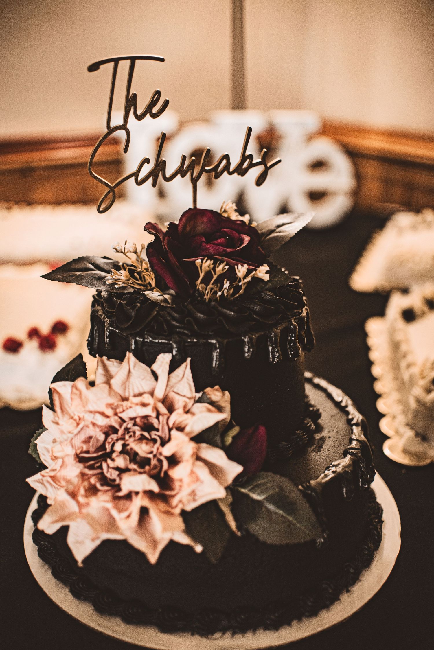 Elegant black wedding cake decorated with burgundy flowers and personalized name topper.