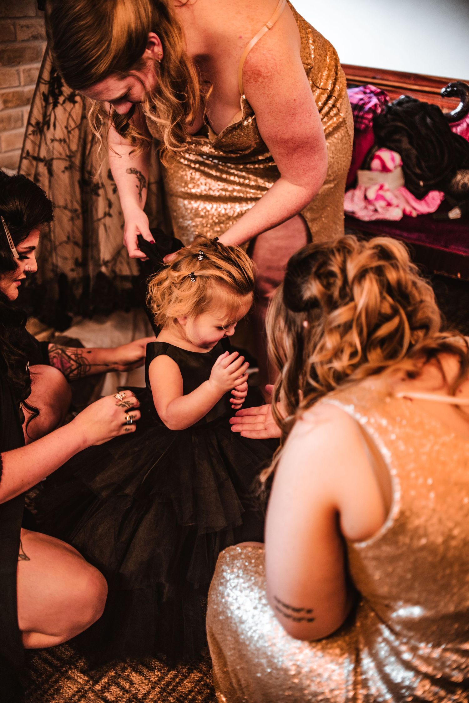 Bridesmaids in gold sequin dresses helping with a young attendant in a black dress.