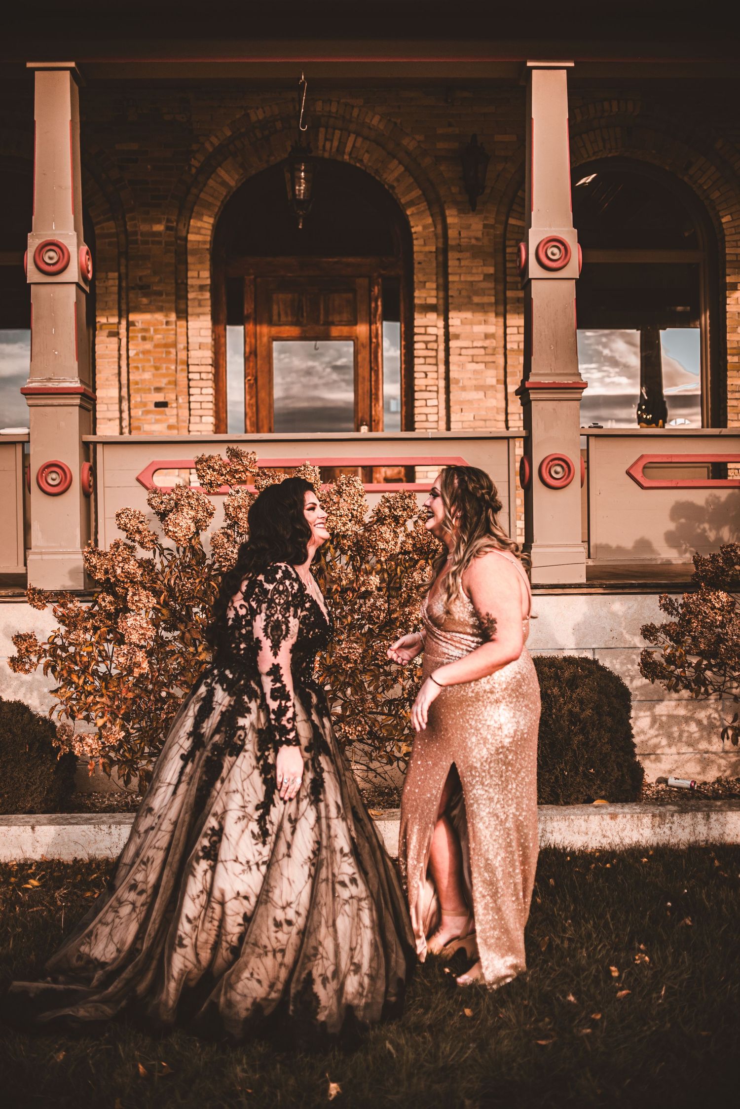 Two people in formal attire stand together against brick building with arched columns.