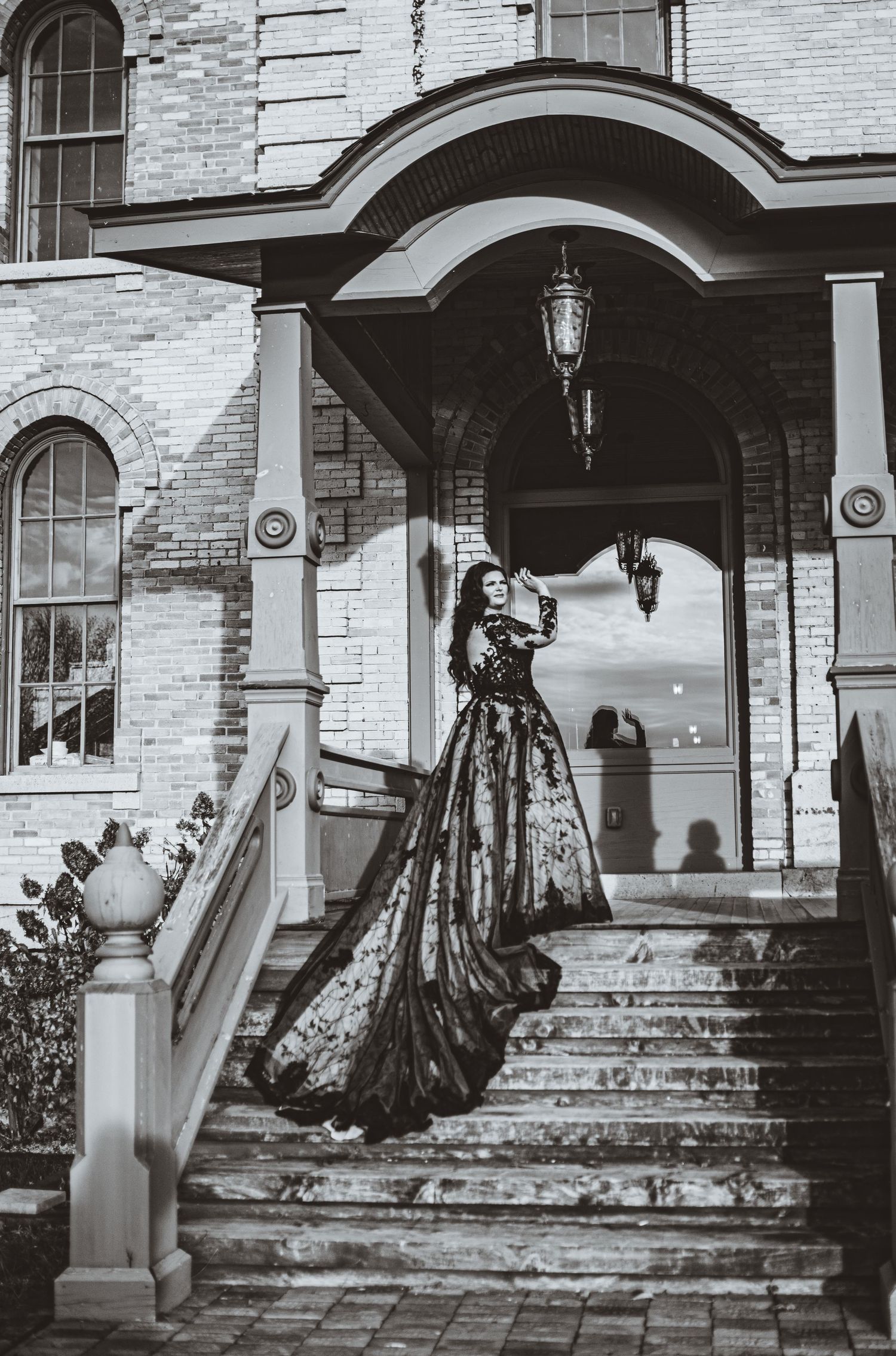 Black and white photo of elegant lace gown with flowing train on historic building steps.