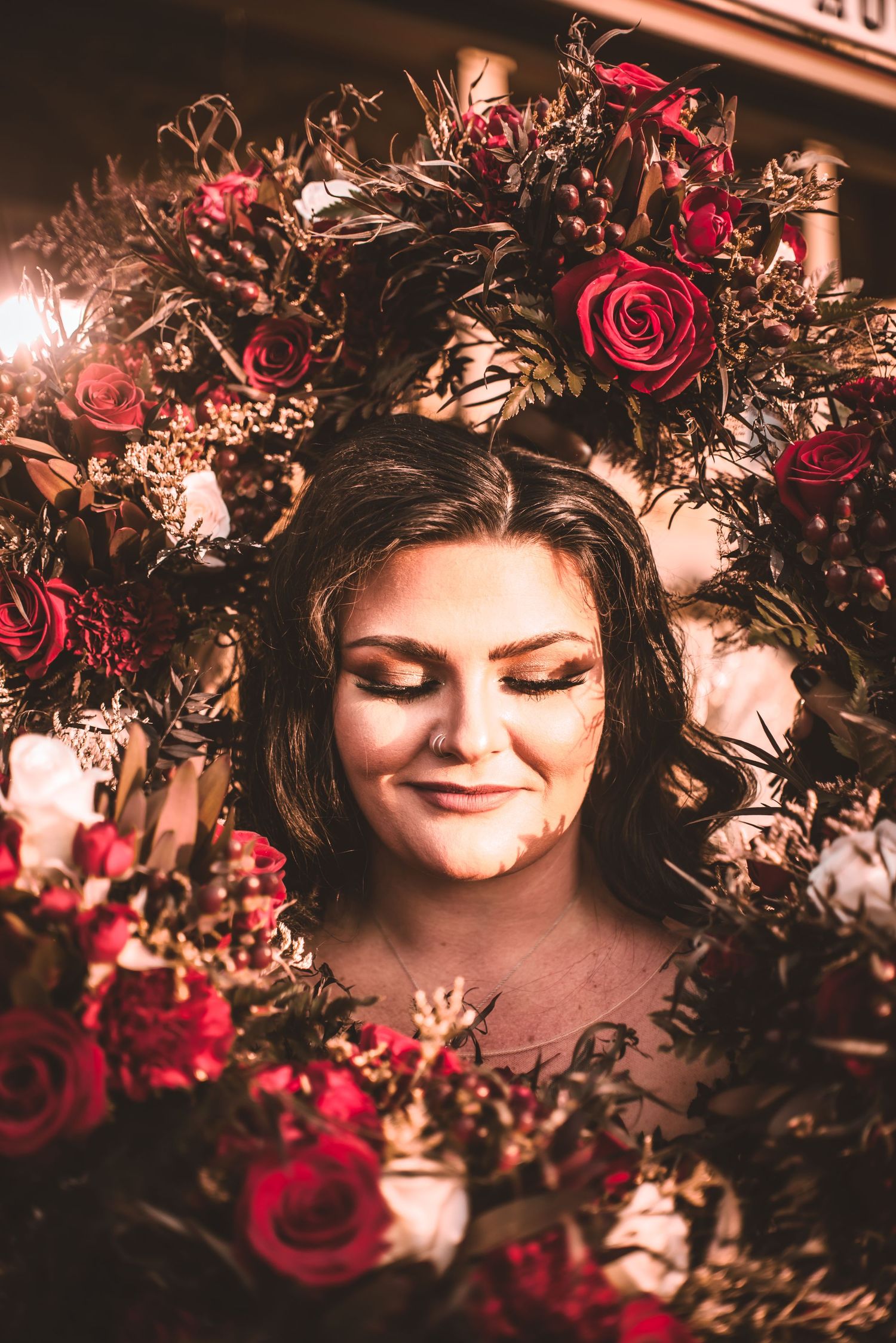 Romantic portrait framed by dark red roses and dried flowers in dramatic lighting.