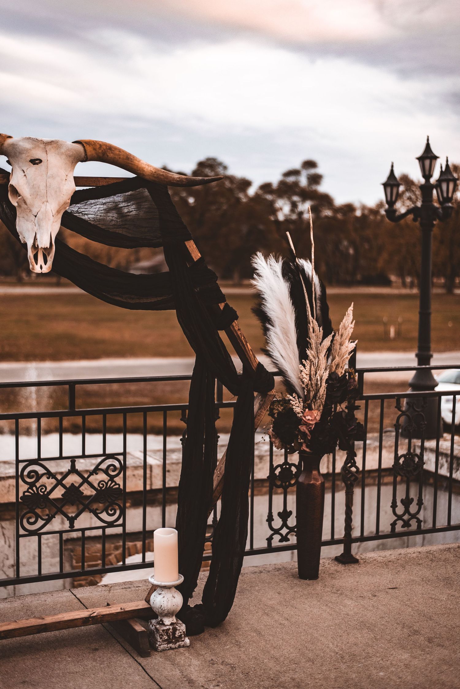 Rustic wedding decor featuring a cattle skull, pampas grass, and wrought iron railing at sunset.