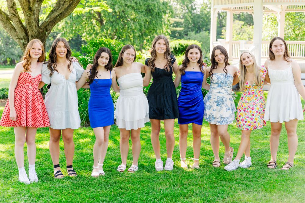 Group of friends in summer dresses posing together in a garden with a white gazebo.