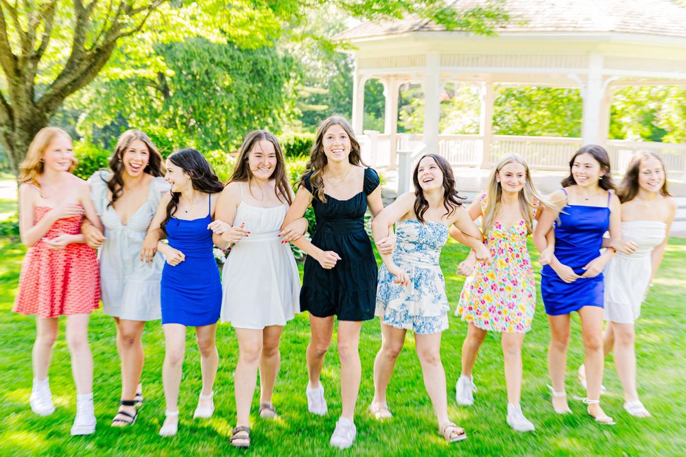 Friends in colorful summer dresses laughing and posing together in a sunny garden setting.