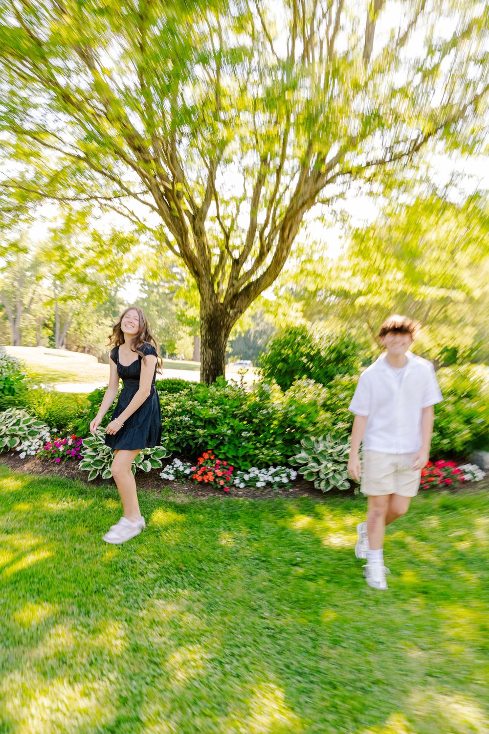 Motion-blurred photo of two people walking on grass with a tree and garden in the background.