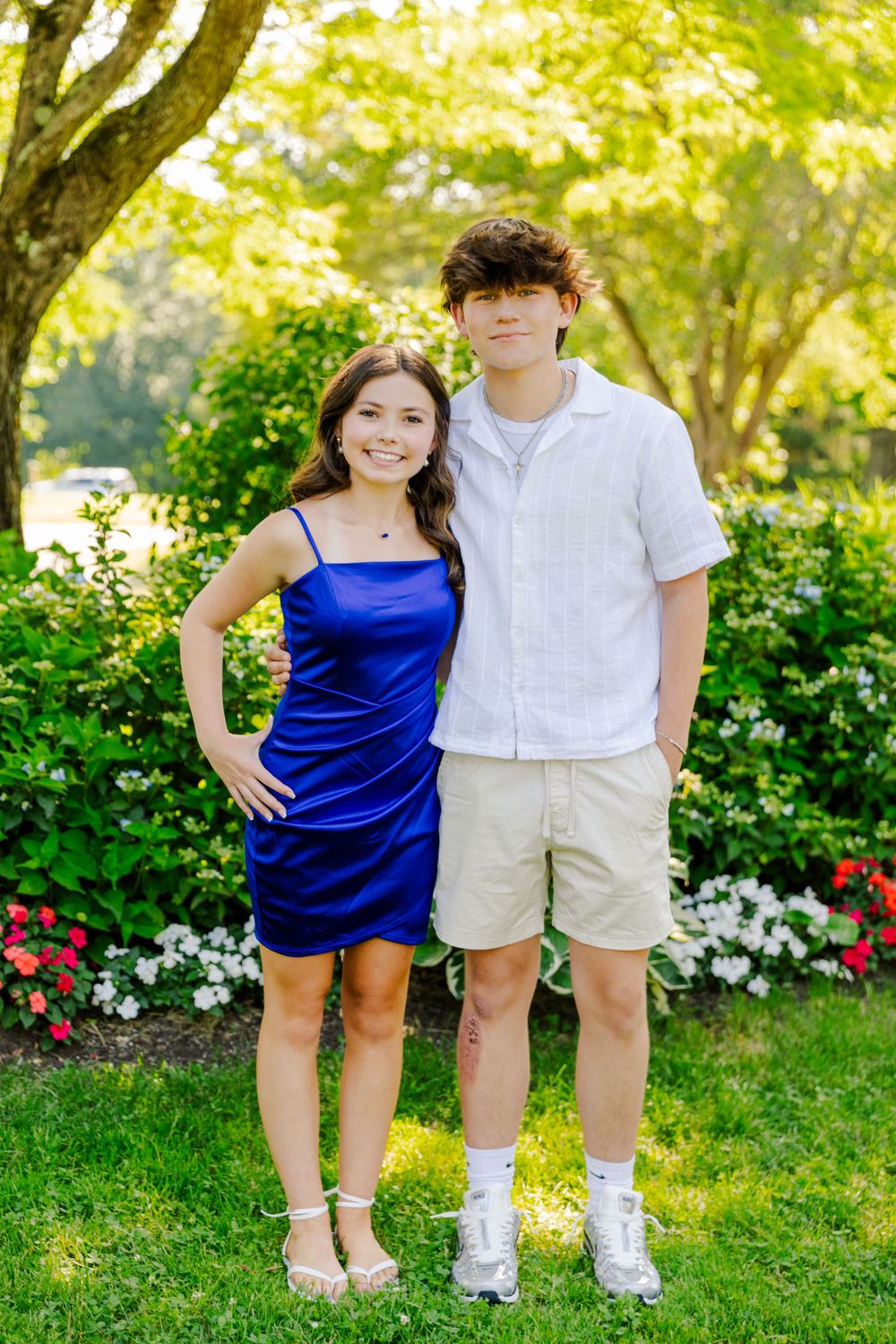 A couple poses together in a lush garden setting with blooming flowers and greenery.