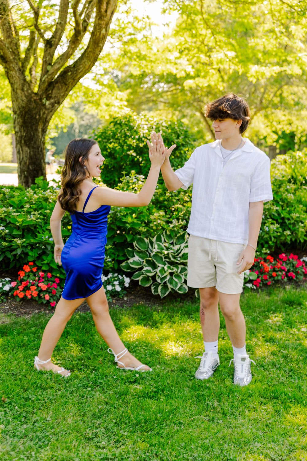 Two people give each other a high-five while standing in a garden setting with blooming flowers.