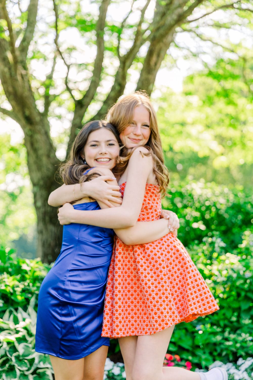 Two friends in blue and orange polka dot dresses embrace while smiling outdoors.