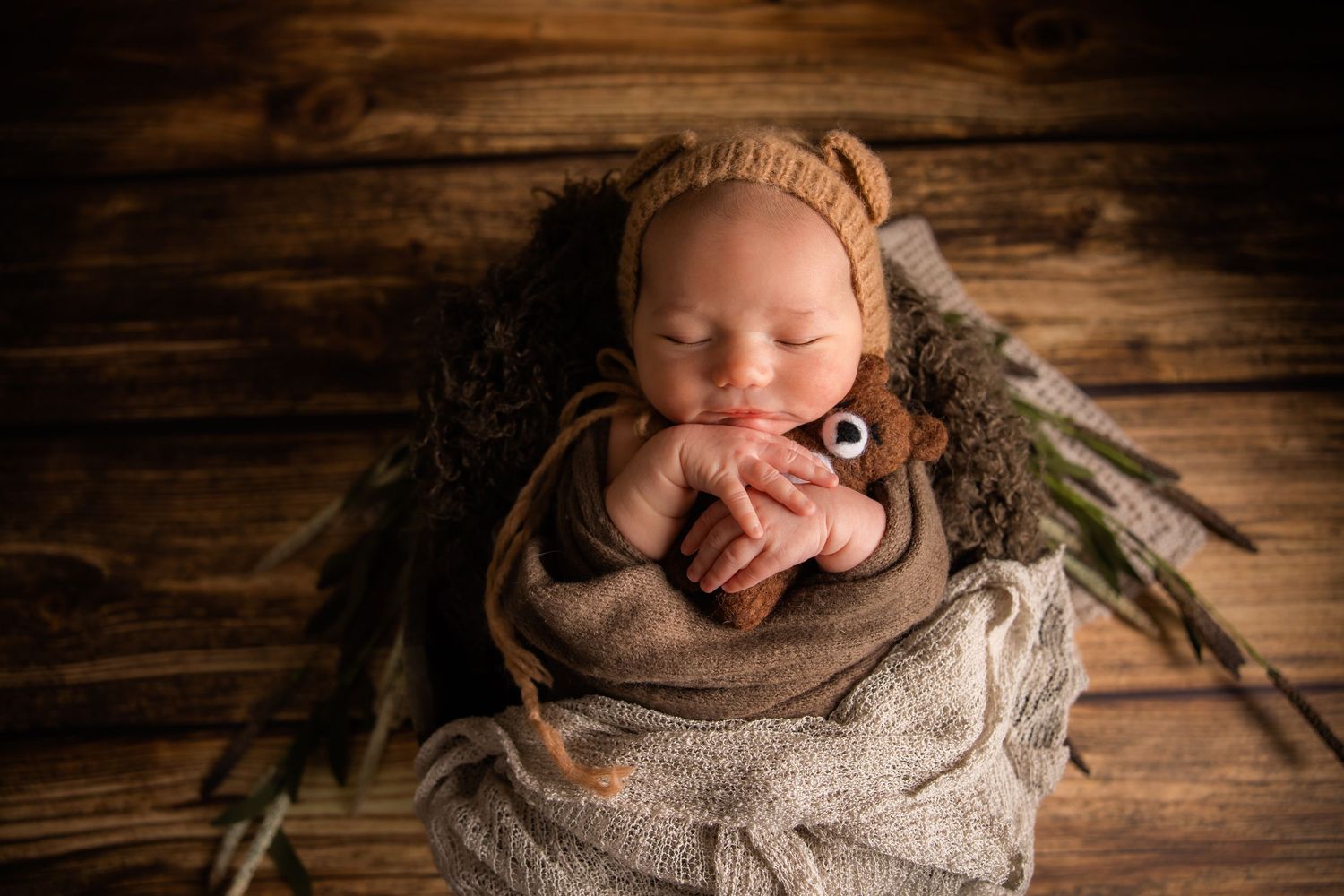 Sleeping newborn wrapped in cozy gray knit blanket on rustic wooden backdrop.
